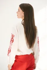 Camisa color crema con bordados florales marrones en las mangas, corte clásico, cuello camisero y cierre frontal con botones.