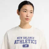 Remera corta color crema de corte holgado con mangas cortas y cuello redondo. Estampado frontal con el logo de New Balance y la palabra "Athletics" en azul.