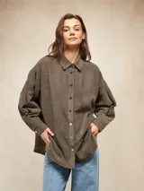 Camisa de pana color oliva, con corte oversize, cuello clásico, cierre frontal con botones metálicos y mangas largas con puños abotonados.
