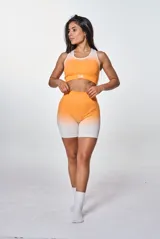 Conjunto deportivo de dos piezas compuesto por un top de cuello redondo y un short de tiro alto, ambos con diseño degradado en tonos naranja y blanco. El top presenta el logo 'bk.' estampado en el frente.