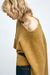Jersey de punto color mostaza con cuello redondo y mangas amplias tipo murciélago. Presenta un diseño ajustado en la cintura con un cinturón fino de cuero sintético en color marrón a contraste.