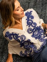 Blusa blanca de algodón con bordados azules, escote en V, cierre frontal con botones y mangas 3/4 dolman.