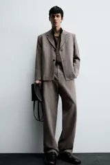 Pantalón de traje de corte slim fit, color marrón con textura sutil. Cuenta con cierre frontal de cremallera y botón, bolsillos laterales y bolsillos traseros de doble vivo con botón.