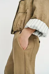 Chaqueta corta de color verde militar, con cuello solapa, bolsillos delanteros con solapa y cierre frontal de botones ocultos. Presenta mangas amplias con vuelta en los puños que muestran un forro a rayas.