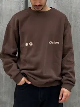 Buzo marrón con logo "Osten" y diseño gráfico de sol en color beige. Corte oversize, cuello redondo y mangas largas.