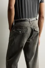 Jeans loose fit de hombre en denim de algodón color gris oscuro con efecto lavado. Presenta perneras con costuras giradas hacia los tobillos, tiro medio, cierre frontal con botones y bolsillos frontales con bolsillo cerillero.