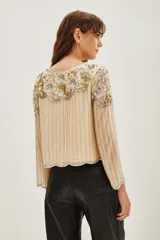 Camisa de manga larga en color crema, con diseño bordado en hilos dorados y plateados que forman líneas verticales y detalles florales en el pecho. Presenta un estilo elegante y sofisticado con aplicaciones brillantes.