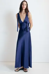 Vestido midi satinado color marrón, con escote en V y tirantes anchos ajustables con lazada en los hombros. Presenta cierre lateral con cremallera oculta.