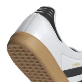 Championes Adidas Samba LT blancos con las tres tiras laterales en negro, refuerzo de gamuza en la puntera y suela de goma color caramelo.