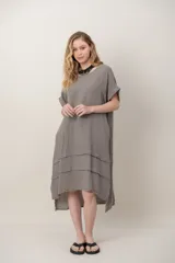 Vestido midi de lino color beige, de corte holgado y silueta acampanada. Cuenta con cuello redondo, mangas cortas amplias, bolsillos laterales y detalles de recortes horizontales en la falda con terminación asimétrica más larga en la parte trasera.