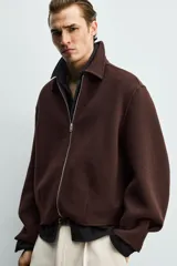 Cazadora boxy fit marrón de corte corto, confeccionada en tejido con mezcla de lana. Presenta cuello camisero, cierre frontal de cremallera metálica, bolsillos de vivo en la cadera y mangas largas.