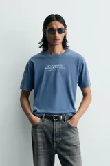 Camiseta relaxed fit de color azul con efecto lavado, cuello redondo y manga corta. Cuenta con un estampado de texto a contraste en el delantero y acabados con efecto rotos.