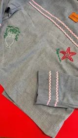 Chaqueta de jean celeste con bordados artesanales y a máquina. Presenta detalles de pespuntes ondulados en rosa y amarillo en el cuello, puños y bolsillos. Los bolsillos frontales tienen bordados de un limón y una figura marina estilizada.
