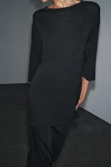 Prenda superior negra de punto liso, con cuello redondo y mangas tres cuartos. Presenta aberturas laterales en el bajo.