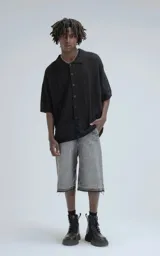 Camisa de manga corta tejida en punto abierto negro, con cuello polo y cierre frontal de botones. Presenta un calce oversize.