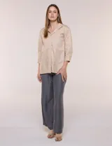 Camisa de silueta holgada y largo extendido, confeccionada en poplín elástico de color blanco. Presenta cuello solapa abierto en V con cartera frontal de abotonadura oculta, hombros caídos y mangas tres cuartos. Cuenta con espalda con canesú, pliegue central y ruedo recto con pequeñas aberturas laterales.