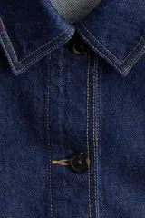 Campera camisera en denim rígido color azul, con cuello camisero, cierre frontal de botones, bolsillos de parche delanteros y bajo redondeado.