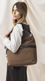 Cartera tipo hobo de tamaño grande en color beige, con detalles en negro. Presenta una franja horizontal negra con el logo de la marca, asa corta de hombro y correa larga desmontable. Incluye bolsillo frontal con cierre oculto y bolsillo trasero.