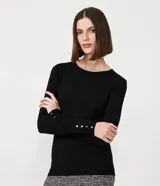 Suéter de punto color rosado, con cuello barco, mangas largas y puños con botones decorativos. El dobladillo también es acanalado.