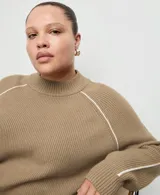 Jersey de punto color tostado con cuello alto y mangas raglán con líneas blancas decorativas en los hombros.