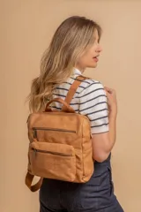 Mochila urbana de tamaño mediano confeccionada en símil cuero color crema. Presenta un diseño estructurado con asa superior, correas ajustables, un compartimento principal con cierre y un bolsillo frontal con cierre y detalle de costuras verticales.