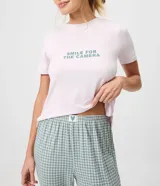 Pijama largo de dos piezas compuesto por una remera rosada de manga corta con cuello redondo y estampa frontal de texto, y un pantalón jogger con cintura elástica y estampado de cuadros vichy en tonos verdes y blancos.