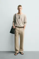 Jersey de punto de corte relajado, con cuello redondo amplio y mangas largas. Presenta un diseño de rayas horizontales finas en contraste sobre fondo beige.