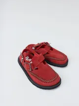 Slipper tipo guillermina confeccionada en gamuza color marrón, con plataforma de goma negra y doble hebilla ajustable. Presenta un pespunte decorativo en el borde inferior y cuenta con interior recubierto en cuero.