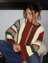 Sweater tejido a mano con terminaciones en crochet, de silueta oversize y mangas acampanadas. Presenta un diseño de rayas verticales multicolores en tonos tierra, rojo, azul y crema.
