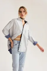 Camisa oversize de algodón con textura de cuadrillé sutil, cuello clásico, bolsillo frontal y mangas largas con puños vueltos que revelan un forro interior a cuadros.