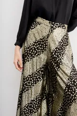 Pantalón de corte amplio y fluido, confeccionado en viscosa jacquard con hilos de lurex. Presenta un diseño de rayas diagonales con estampado de puntos dorados sobre fondo negro, cintura con elástico en la parte trasera y forrería a tono.