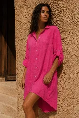 Vestido camisero corto de lino color naranja, con mangas largas arremangables mediante tira con botón, cierre frontal con botones y diseño amplio de corte asimétrico con la parte trasera más larga.