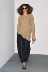 Top de manga larga color beige, con textura fruncida en todo el cuerpo y mangas. Presenta cuello redondo y bajo asimétrico con aberturas laterales ajustables con cordones.