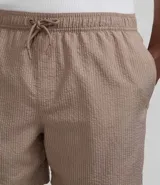 Bermuda de baño color beige, confeccionada en tejido ana ruga texturizado. Tiene lazo en la cintura, bolsillos laterales y un bolsillo trasero.