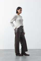 Pantalón de corte recto y pierna amplia confeccionado en símil cuero color marrón oscuro. Presenta una silueta estructurada con costuras verticales frontales que definen su diseño.