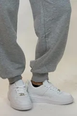 Pantalon deportivo tipo babucha de color beige, con cintura elástica ajustable mediante cordón y puños elásticos en los tobillos.