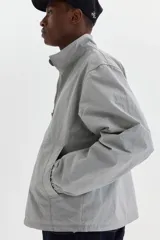 Campera rompevientos de nylon color gris, repelente al agua, con cuello elevado, cierre frontal y bolsillos laterales con botón a presión oculto.