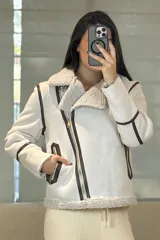 Campera tipo gamulán de color crema con interior y cuello de corderito sintético. Presenta cierre frontal cruzado, bolsillos laterales con cierre y detalles de costuras en contraste color marrón oscuro.