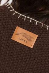 Ruana marrón chocolate tejida, con detalles bordados a mano en los bordes y flecos en el ruedo inferior.