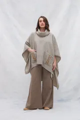Poncho de lana color beige con cuello alto, bolsillos frontales y detalle de cordones de cuero en los bordes de los bolsillos.