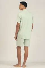 Camisa de manga corta celeste con rayas verticales blancas, cuello clásico, cierre frontal con botones y bolsillo de parche en el pecho.