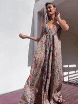 Vestido largo de estilo boho, con estampado tipo paisley en tonos tierra, turquesa y rosa. Presenta un escote profundo con tirantes finos y detalles de bordados florales en color rojo y verde a lo largo del frente.