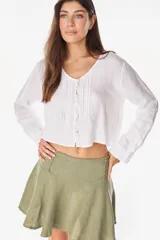 Camisa blanca de lino italiano, de manga larga, escote en V y cierre frontal con múltiples botones y detalles de alforzas.