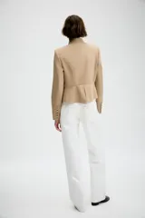 Blazer entallado de sarga color beige con cuello subido y escote en pico. Presenta manga larga con hombreras, detalle de botones metálicos decorativos en el frente y cierre frontal con gancho metálico. Incluye falsos bolsillos de vivo y abertura en la espalda.