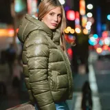 Campera puffer verde con capucha y cuello alto. Tiene cierre frontal con cremallera y botones a presión. Cuenta con dos bolsillos externos y sistema de ajuste regulable en la parte baja. Es acolchada, liviana y de corte regular.