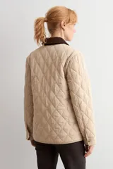 Campera capitoneada de diseño acolchado con patrón de rombos, color beige claro. Presenta cuello camisero de pana en color marrón oscuro, cierre frontal con botones metálicos y bolsillos frontales de parche.