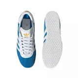 Championes adidas modelo Gazelle edición especial Real Madrid, confeccionados en gamuza azul con las icónicas tres tiras laterales en blanco. Presentan el nombre del club en letras doradas sobre el lateral y suela de goma blanca.