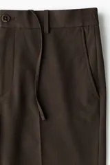 Pantalón de corte relajado color marrón, con cierre de botón, cintura con elástico y cordón interno, bolsillos laterales al bies y bolsillos traseros ribeteados con botón.