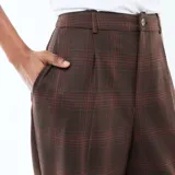 Pantalón marrón de corte ancho y talle alto, con estampado a cuadros y pinzas en la parte delantera.