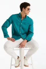 Camisa de lino de manga larga color verde turquesa, con cuello camisero, cierre frontal de botones y un bolsillo ojal en el pecho.